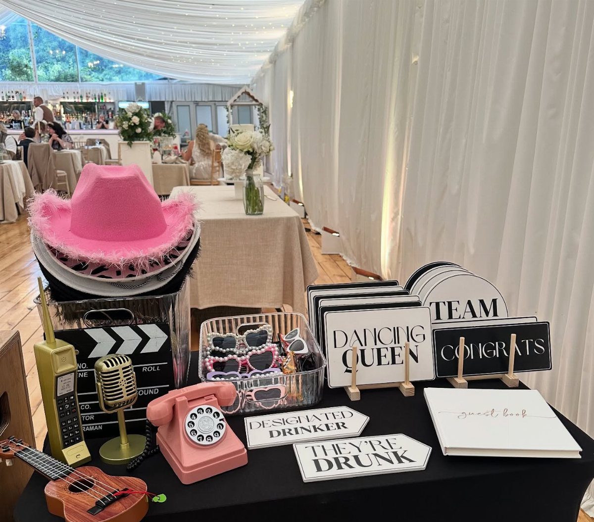 Photo booth props including a pink cowboy hat and funny handheld wedding signs.