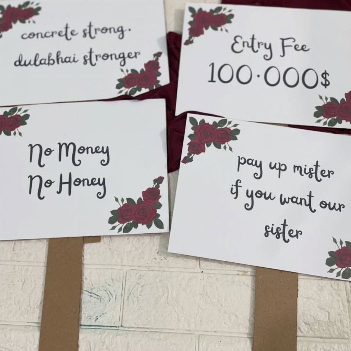 Four humorous wedding signs with red roses and black text on white cards.