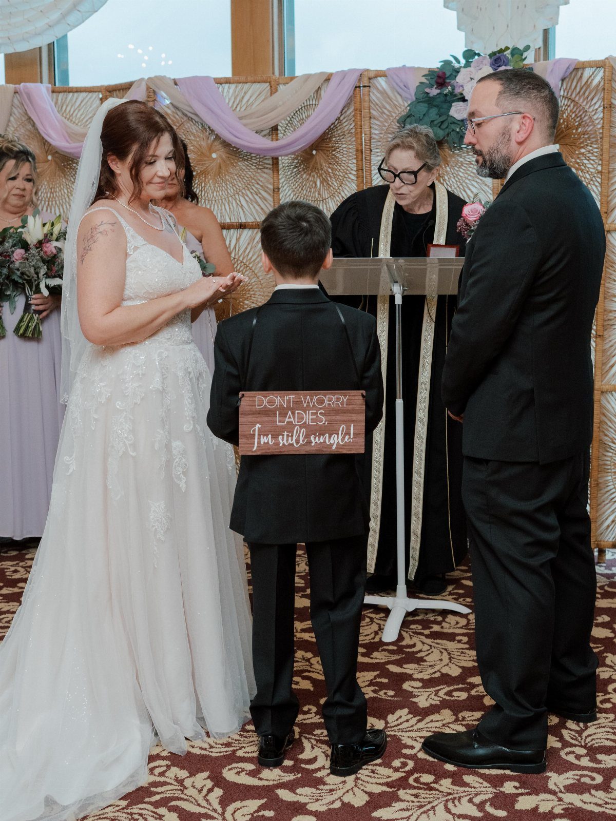 Young ring bearer wearing a funny wooden sign during a wedding ceremony.