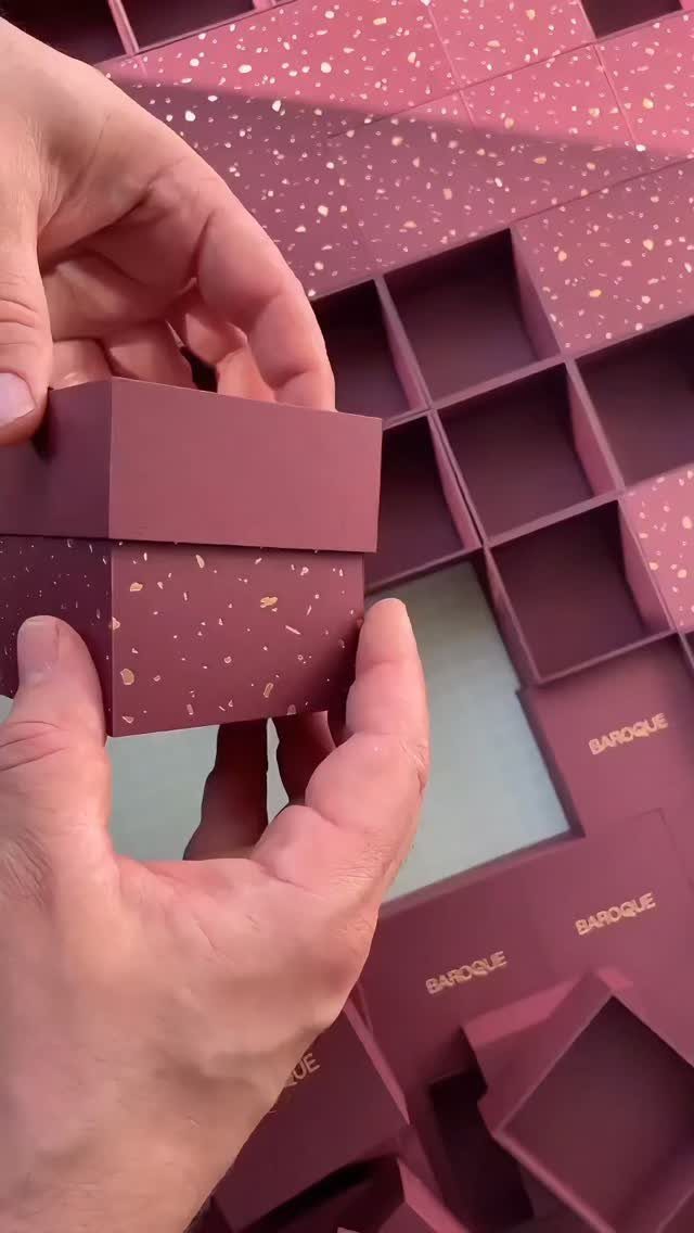 Burgundy gift boxes with gold speckles held by hands among many others.