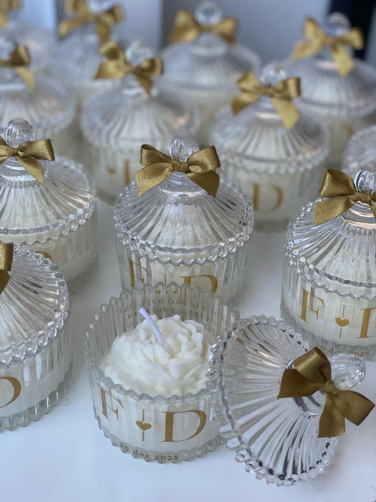 White wax candles in ribbed glass jars with gold lettering and gold bows.