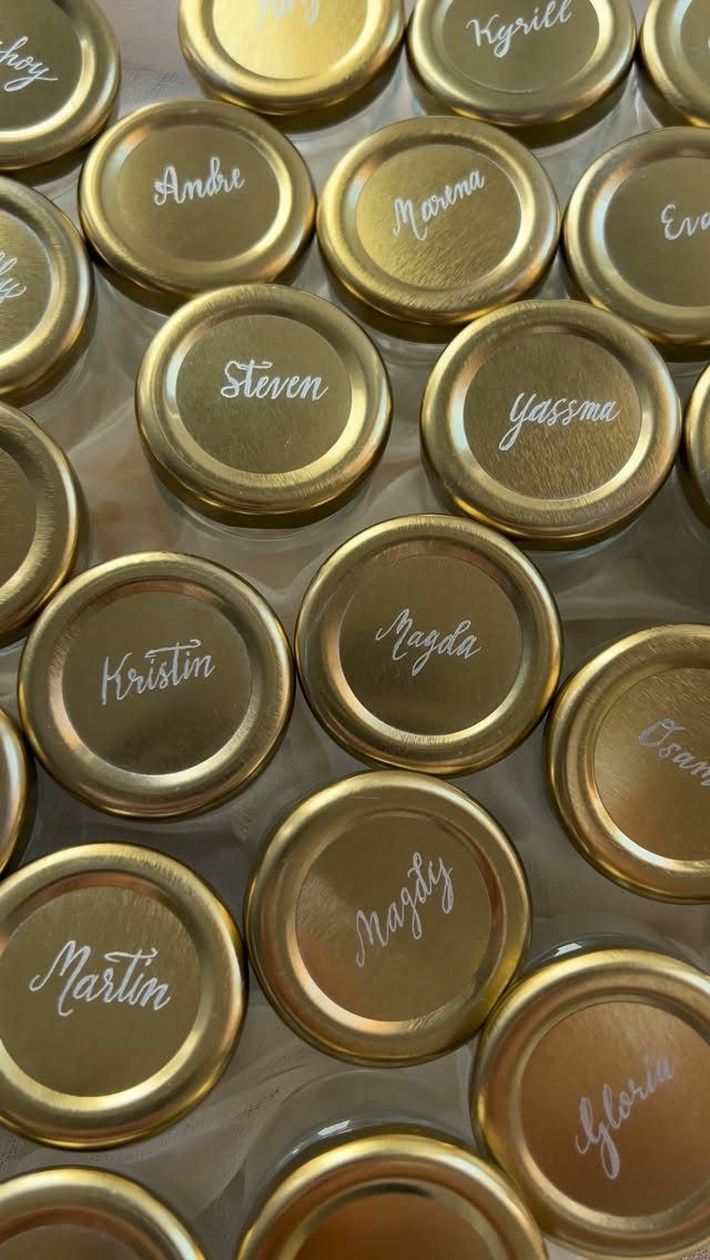 Gold jar lids with personalized names written in white cursive script for wedding favors