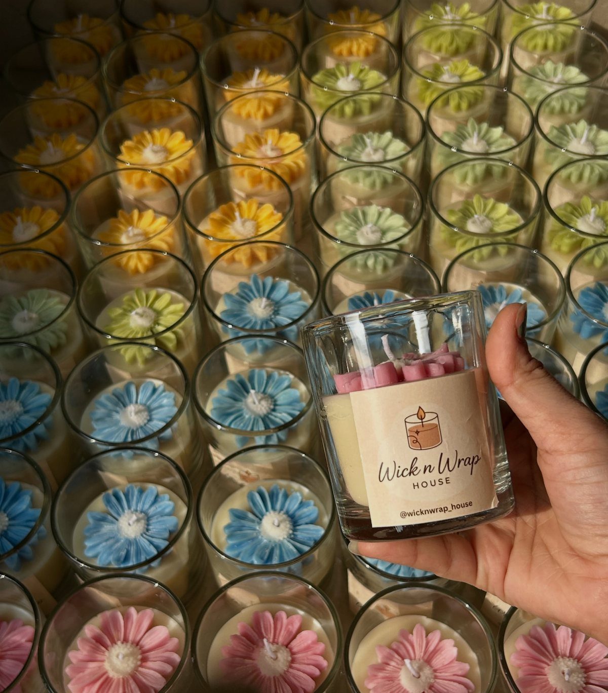 Hand holding a small glass jar candle with a pink wax flower topper.