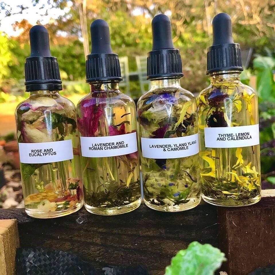 Four glass dropper bottles containing infused oils with dried herbs and floral petals.