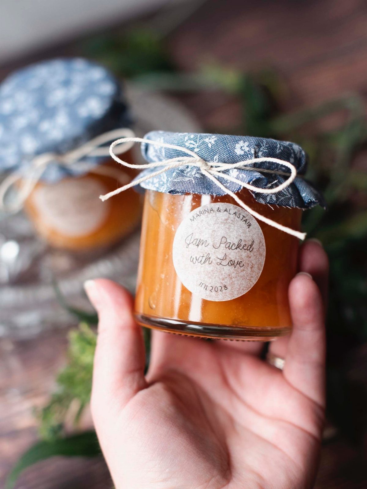 Small glass jar of orange jam with floral fabric lid and custom label.