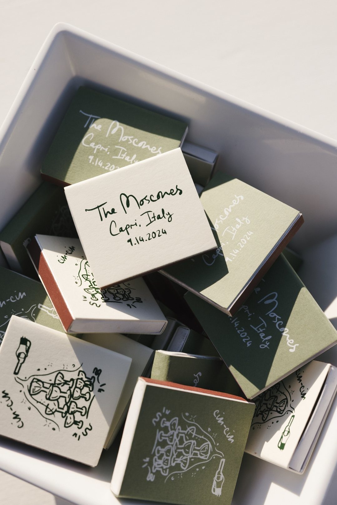 Custom matchboxes in olive green and white inside a white ceramic bowl.