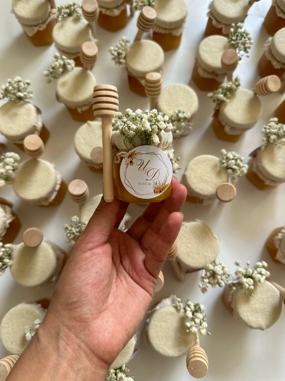Mini honey jars with fabric lids and wooden dippers as wedding favors.