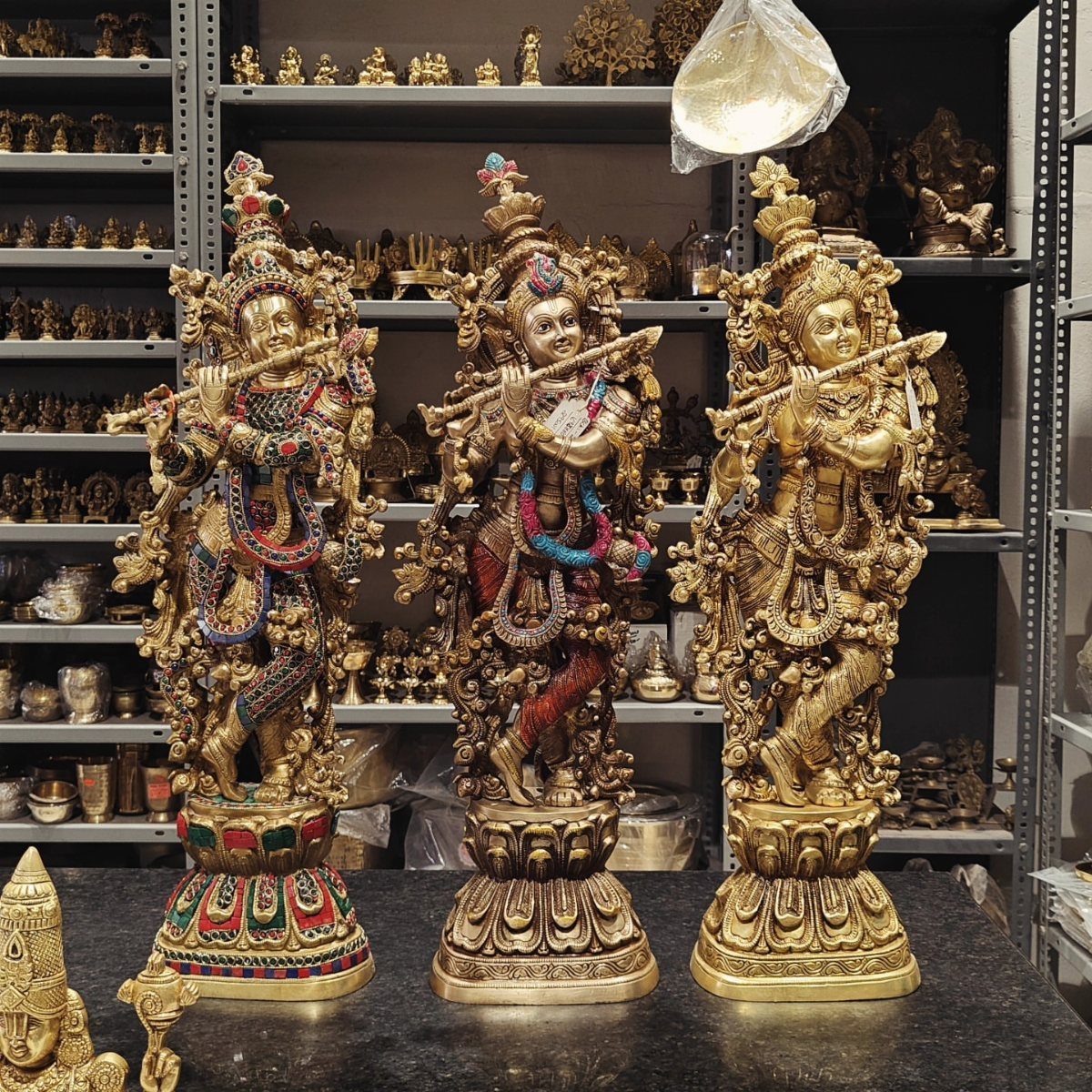 Three ornate brass Krishna statues playing flutes on a store display shelf