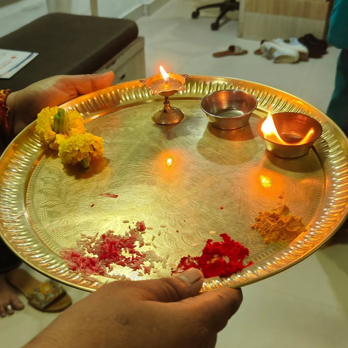 Brass pooja thali with lit diyas, marigold flowers, and colorful ritual powders.
