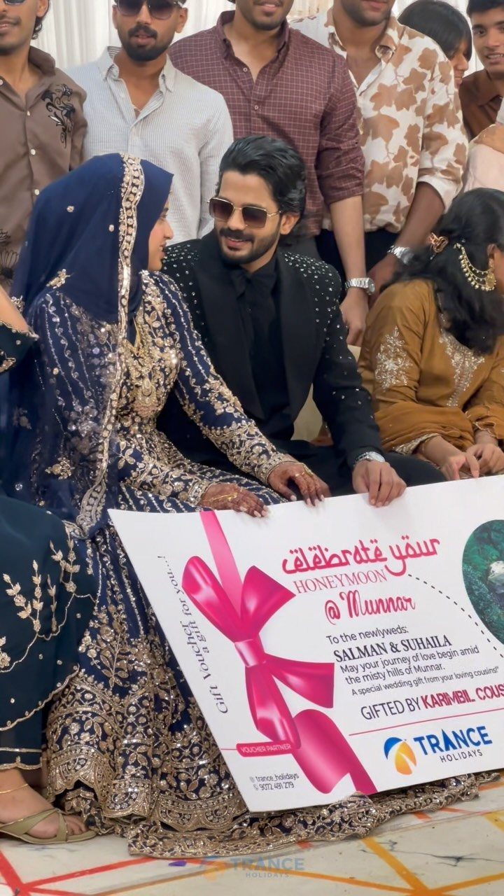 Couple in wedding attire holding a large honeymoon travel gift voucher for Munnar.