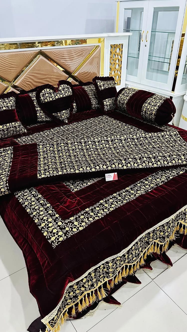 Maroon and gold luxury bedding set with embroidered quilt and decorative pillows.