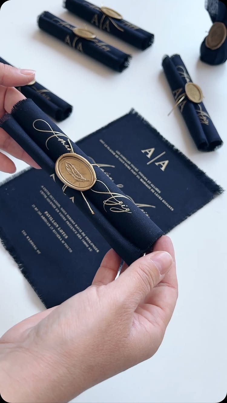 Navy blue fabric wedding invitations with gold lettering and wax seal accents.
