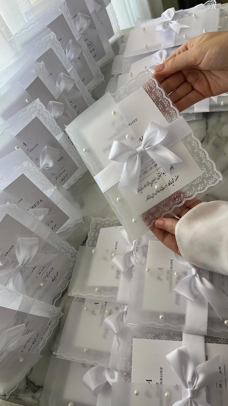 White wedding invitation with a satin bow, lace edges, and pearl accents.