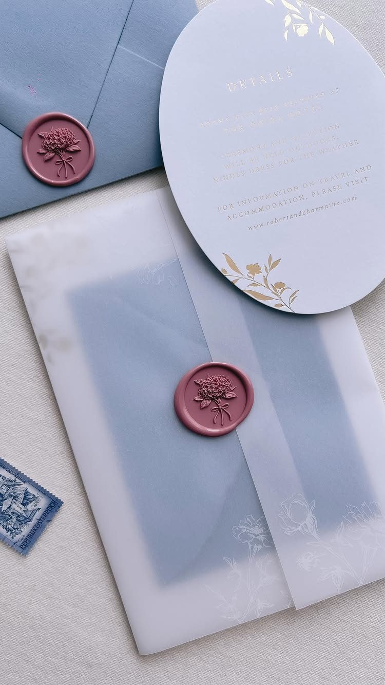 Wedding invitation set with blue envelopes, vellum wrap, and burgundy wax seals.
