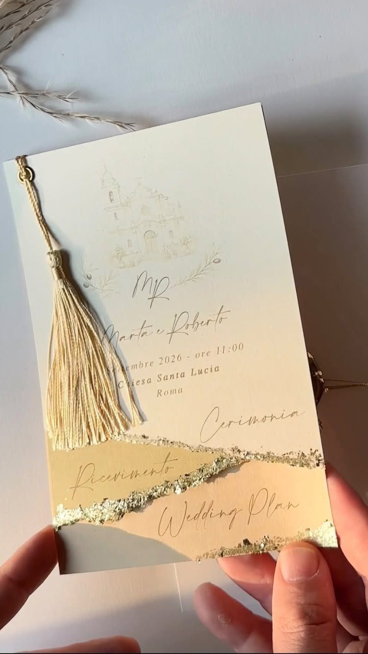 Wedding invitation with gold foil, a tassel, and Italian text held by hands.