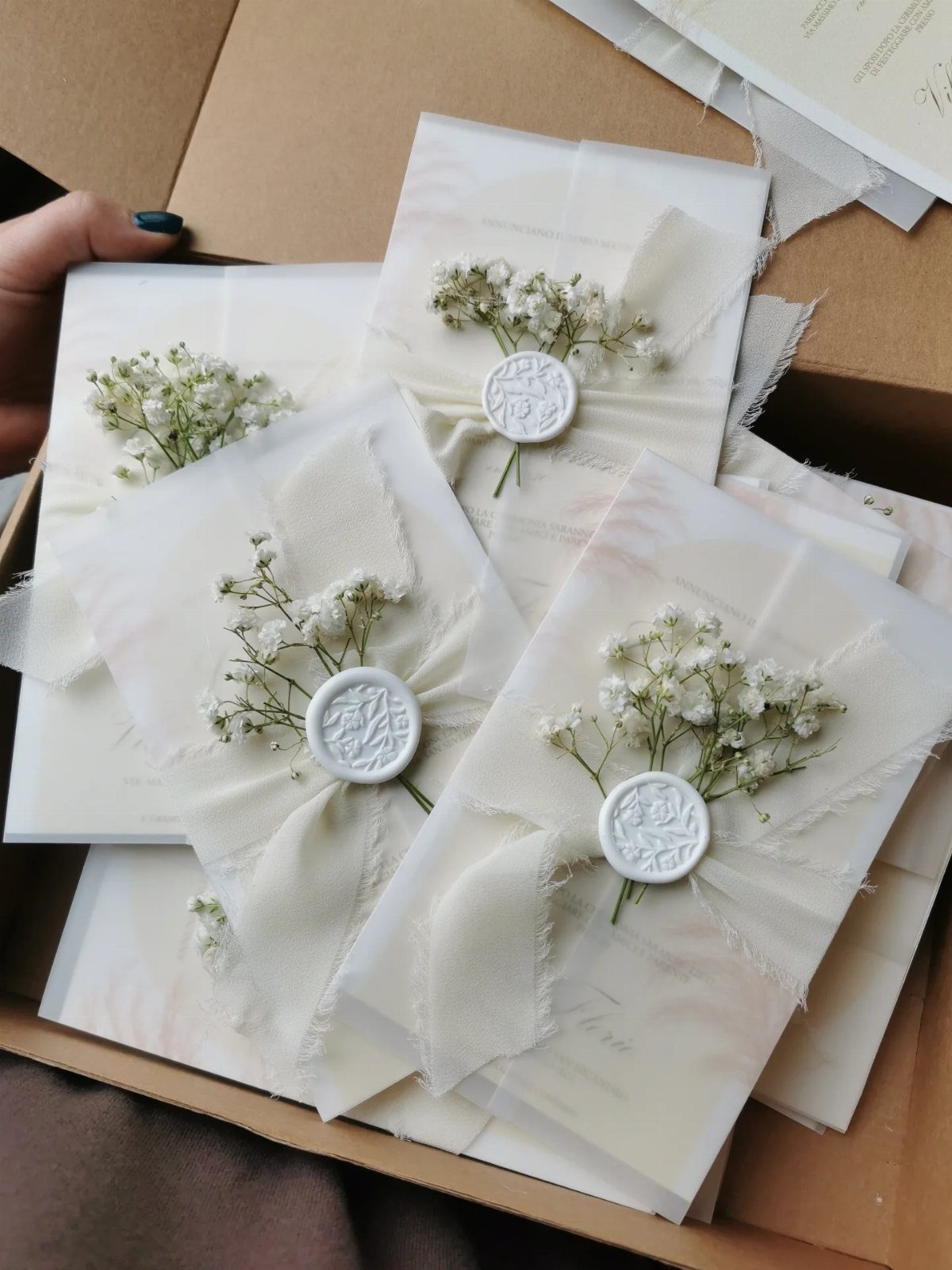 White wedding invitations wrapped in vellum and ribbon with wax seals and baby's breath.