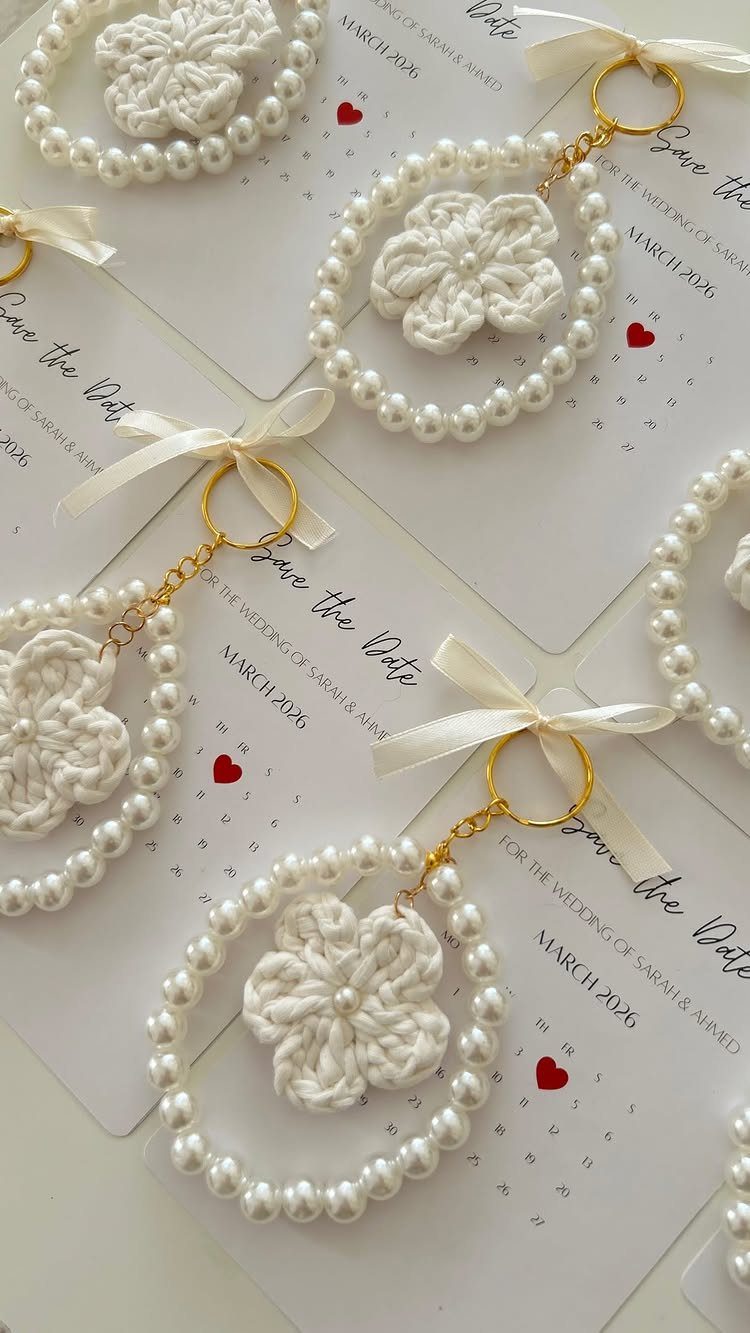 Pearl-beaded keychains with crocheted flowers resting on wedding save the date cards.