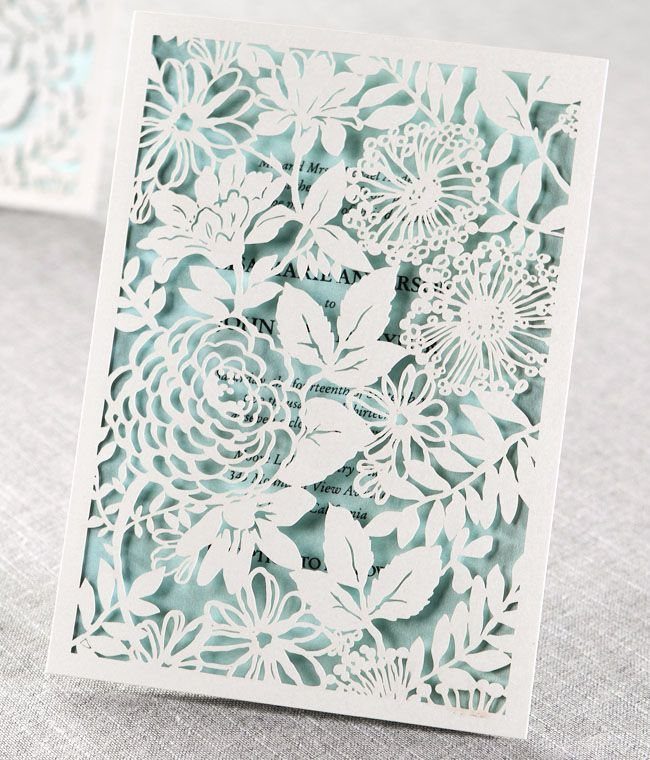 White laser-cut floral invitation overlay on a light lavender background with text.