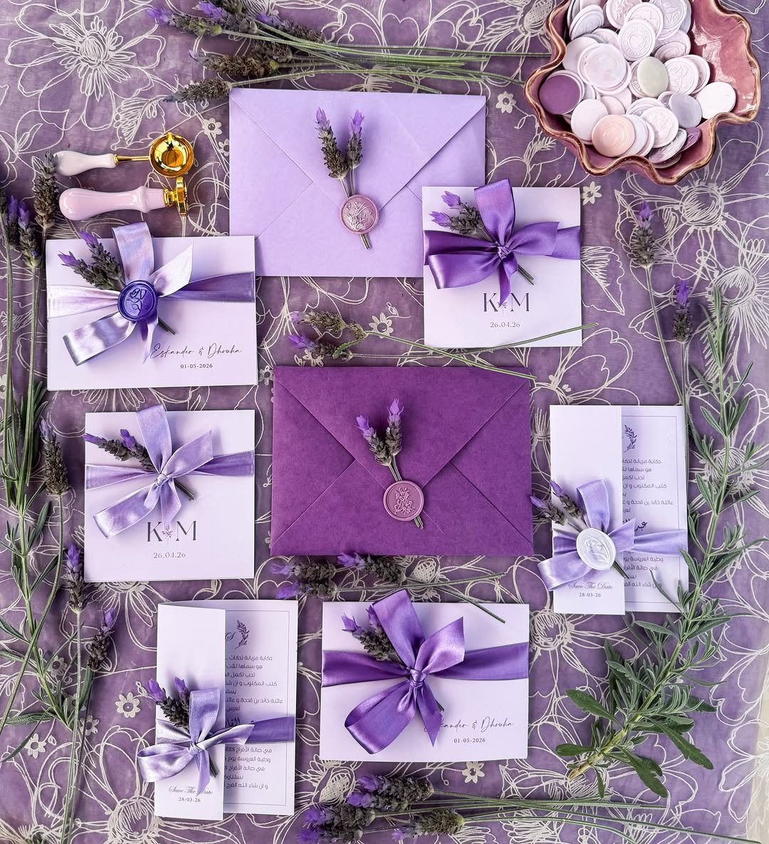 Purple and white wedding invitations with lavender sprigs, ribbons, and wax seals.