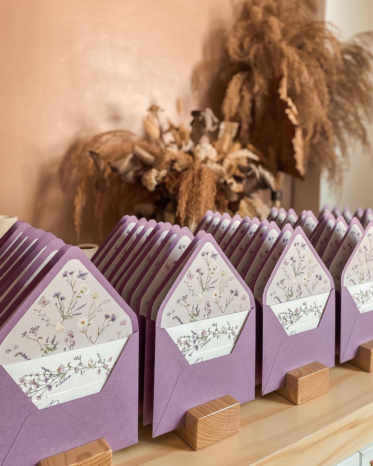 Purple envelopes with lavender floral linings displayed on small wooden blocks.