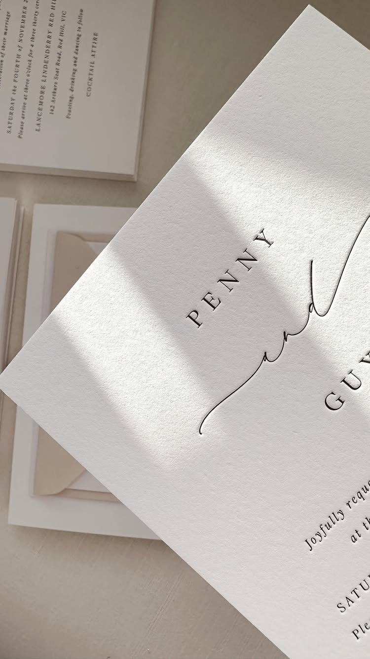 White textured wedding invitations with debossed black typography and elegant script lettering.