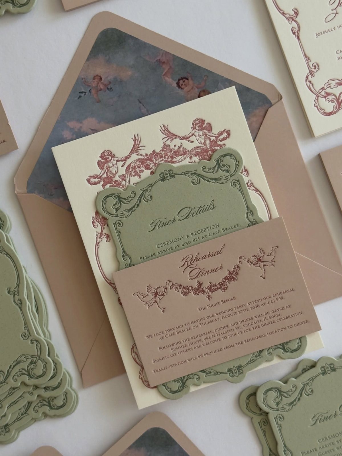 Sage green wedding invitations with red cherub illustrations and elegant cursive typography.