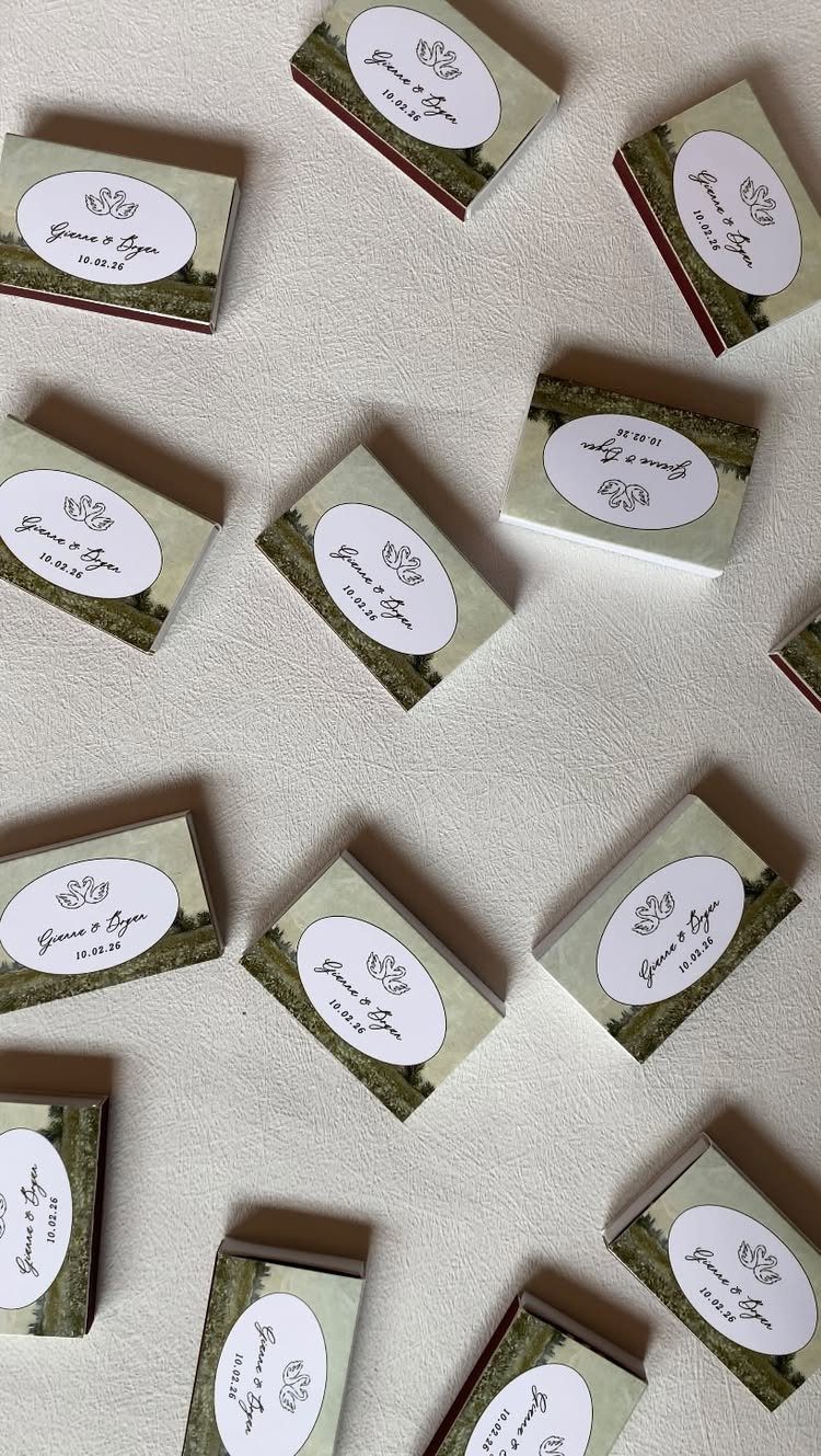 Custom wedding matchboxes with personalized oval labels scattered on a white surface.