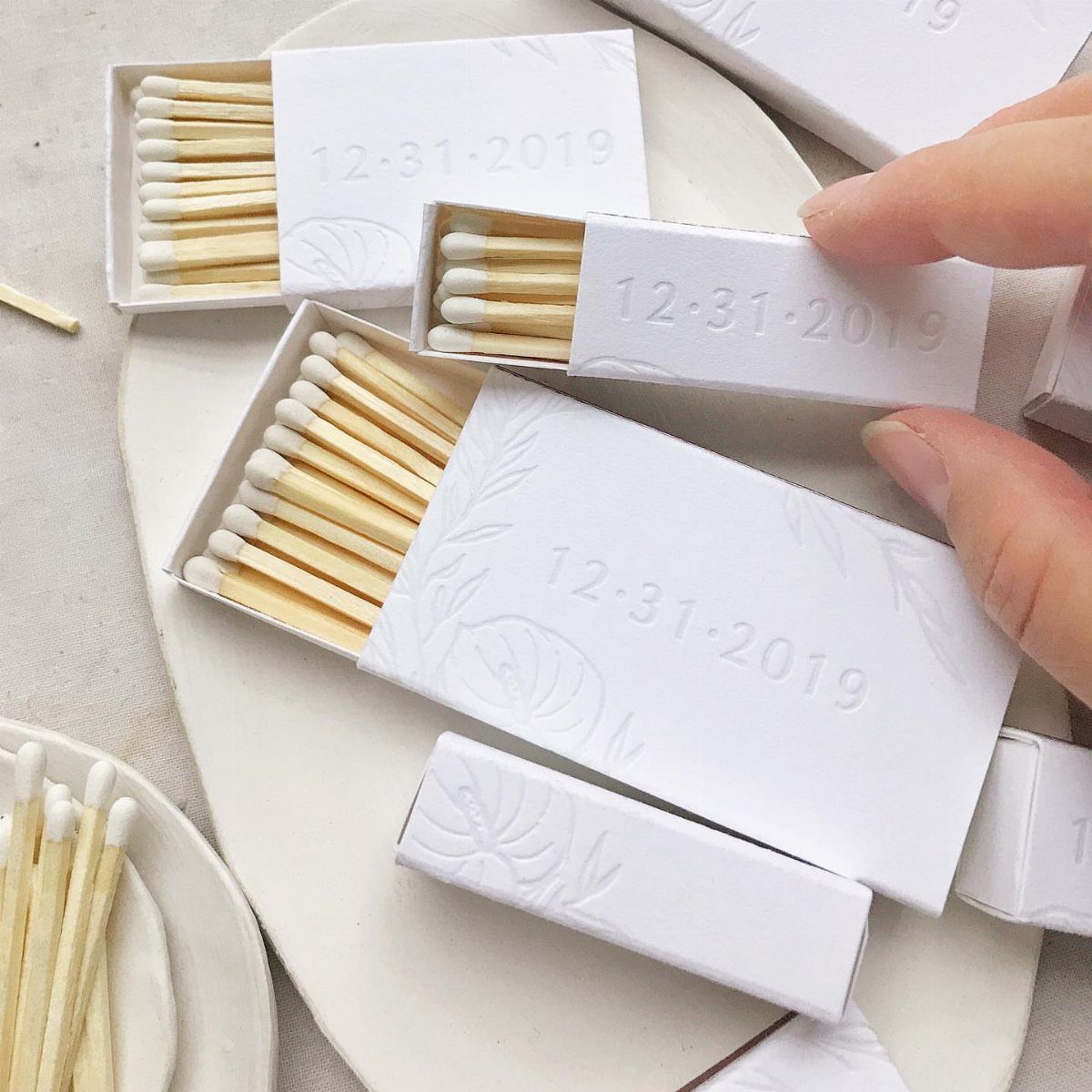 White matchboxes with embossed floral designs and a date on a ceramic plate.