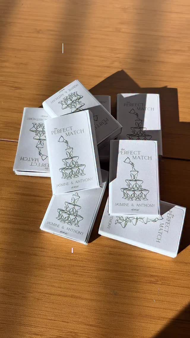 White wedding matchbooks with cake illustrations scattered on a wooden table.