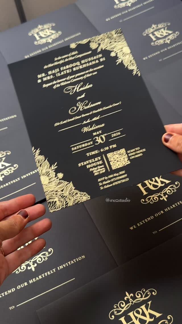 Black wedding invitation card with gold foil lettering and floral corner decorations.