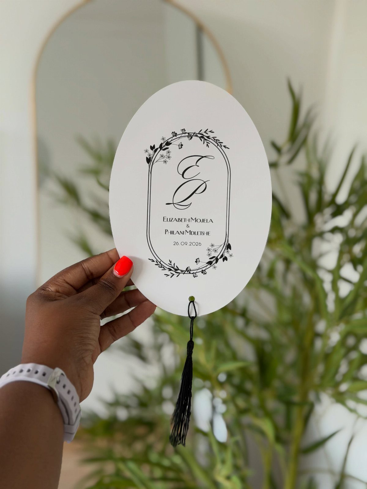Oval white wedding card with black botanical leaf drawings and elegant calligraphy.