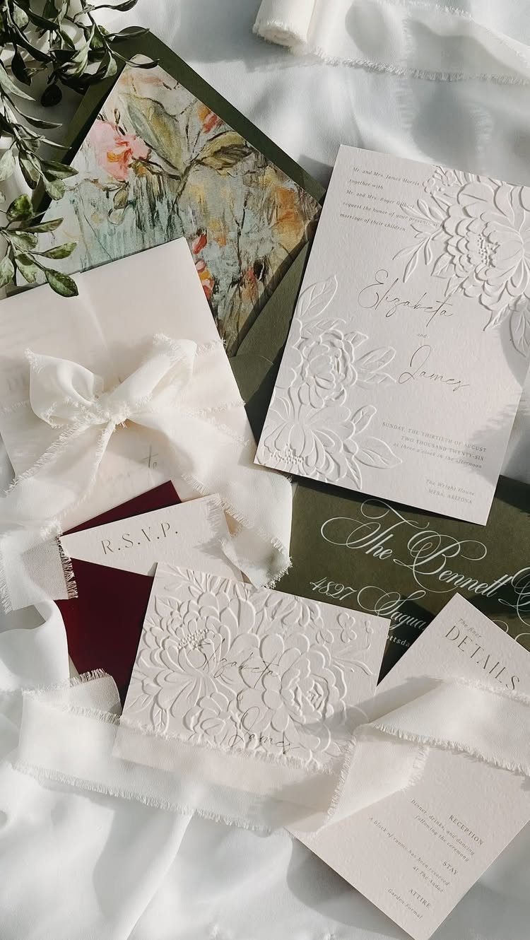 White embossed wedding invitation cards with ribbons on a white fabric background.