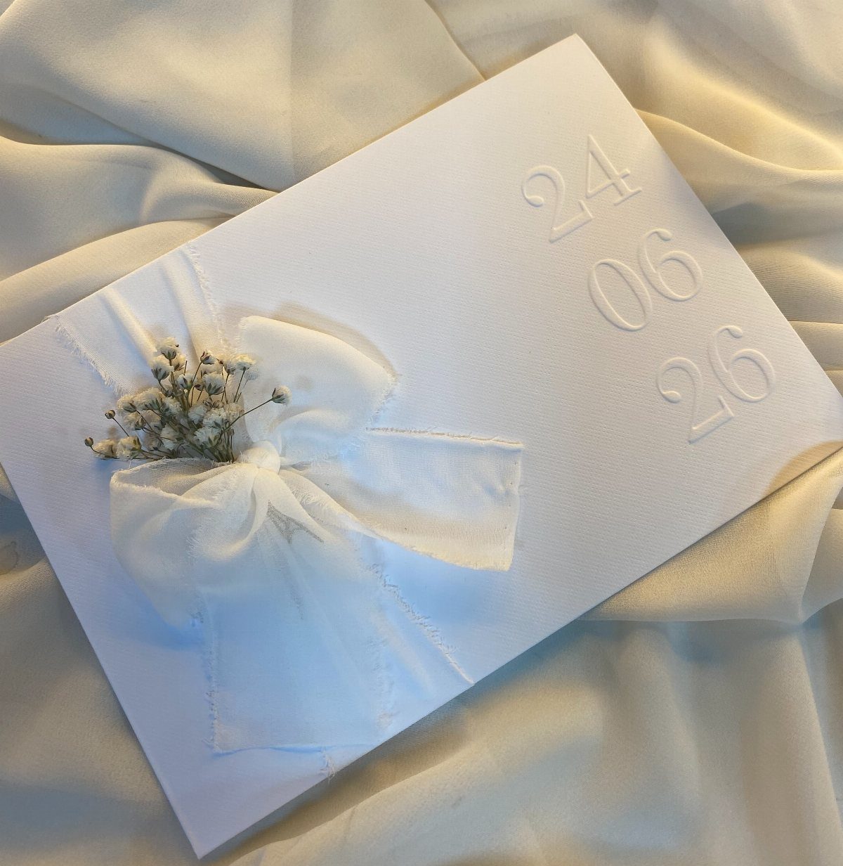 White embossed wedding card with a sheer ribbon bow and dried baby's breath flowers.