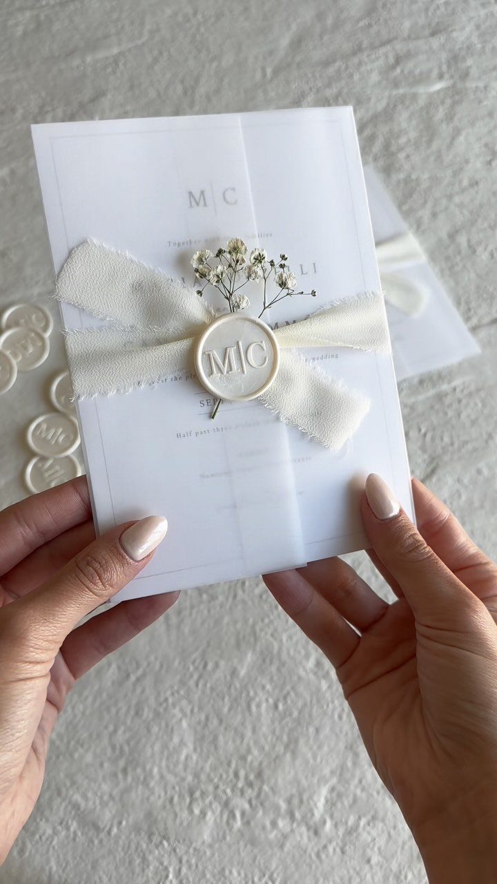 Minimalist white wedding invitation card with a ribbon, wax seal, and baby's breath.
