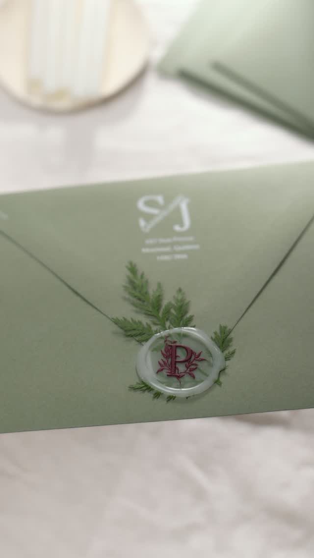 Sage green envelope with a white wax seal and a small green sprig.