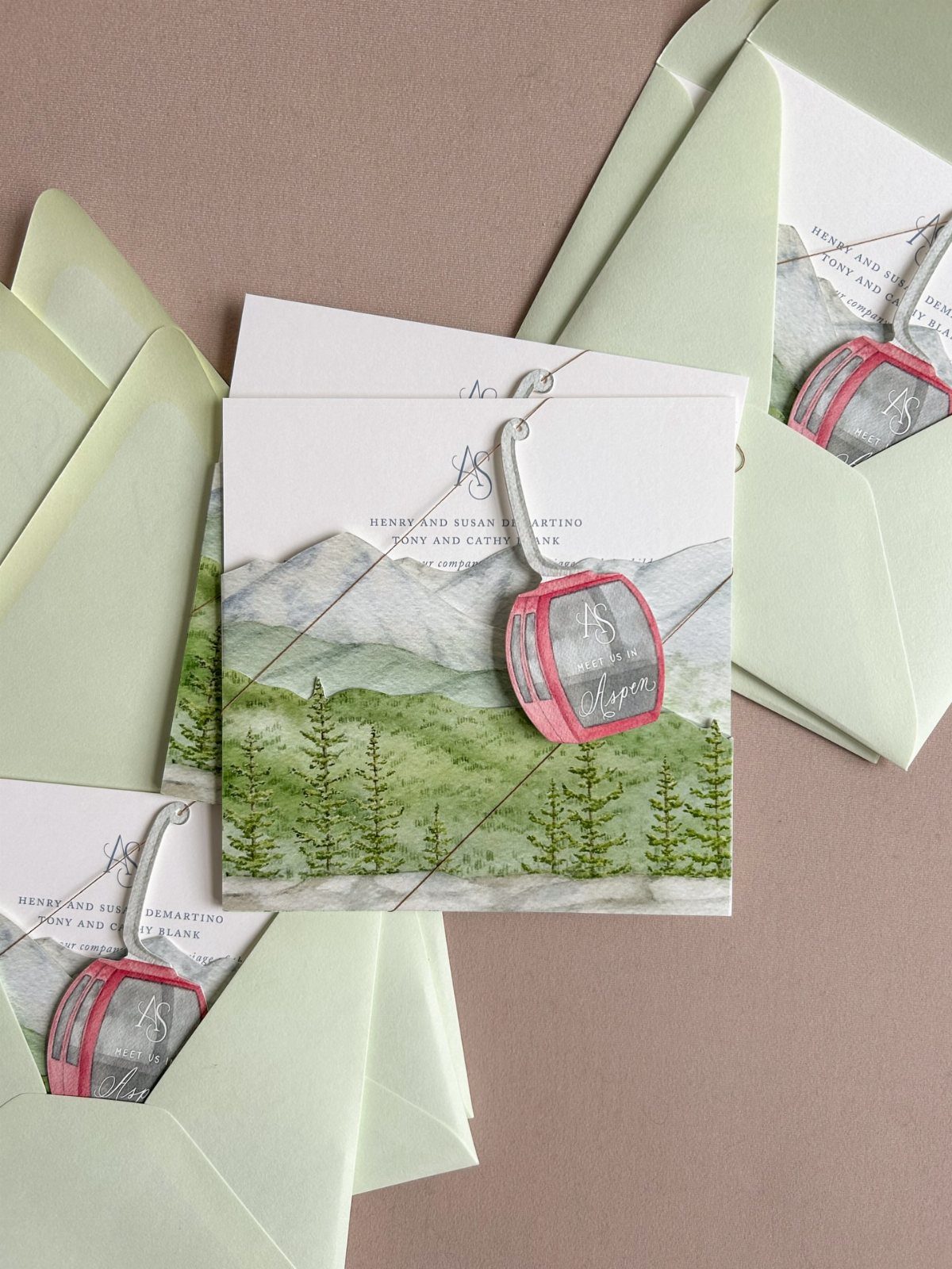 Mountain wedding invitations with watercolor landscapes and small pink gondola charms.