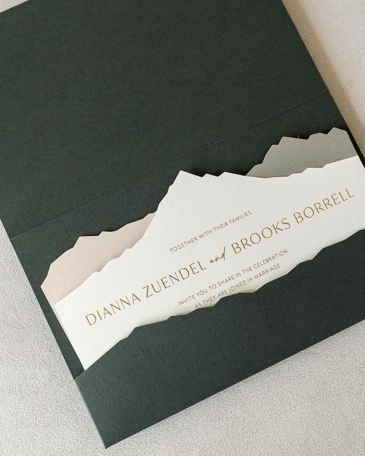 Wedding invitation with mountain silhouette edge inside a dark green envelope