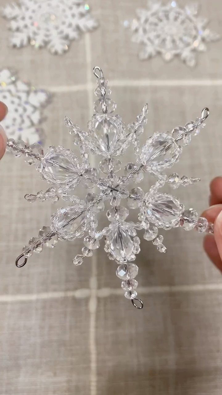 Clear beaded crystal snowflake ornament held against a background of white lace snowflakes.