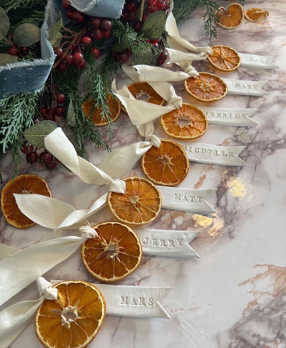 Dried orange slice ornaments with personalized name tags and white ribbons on marble.