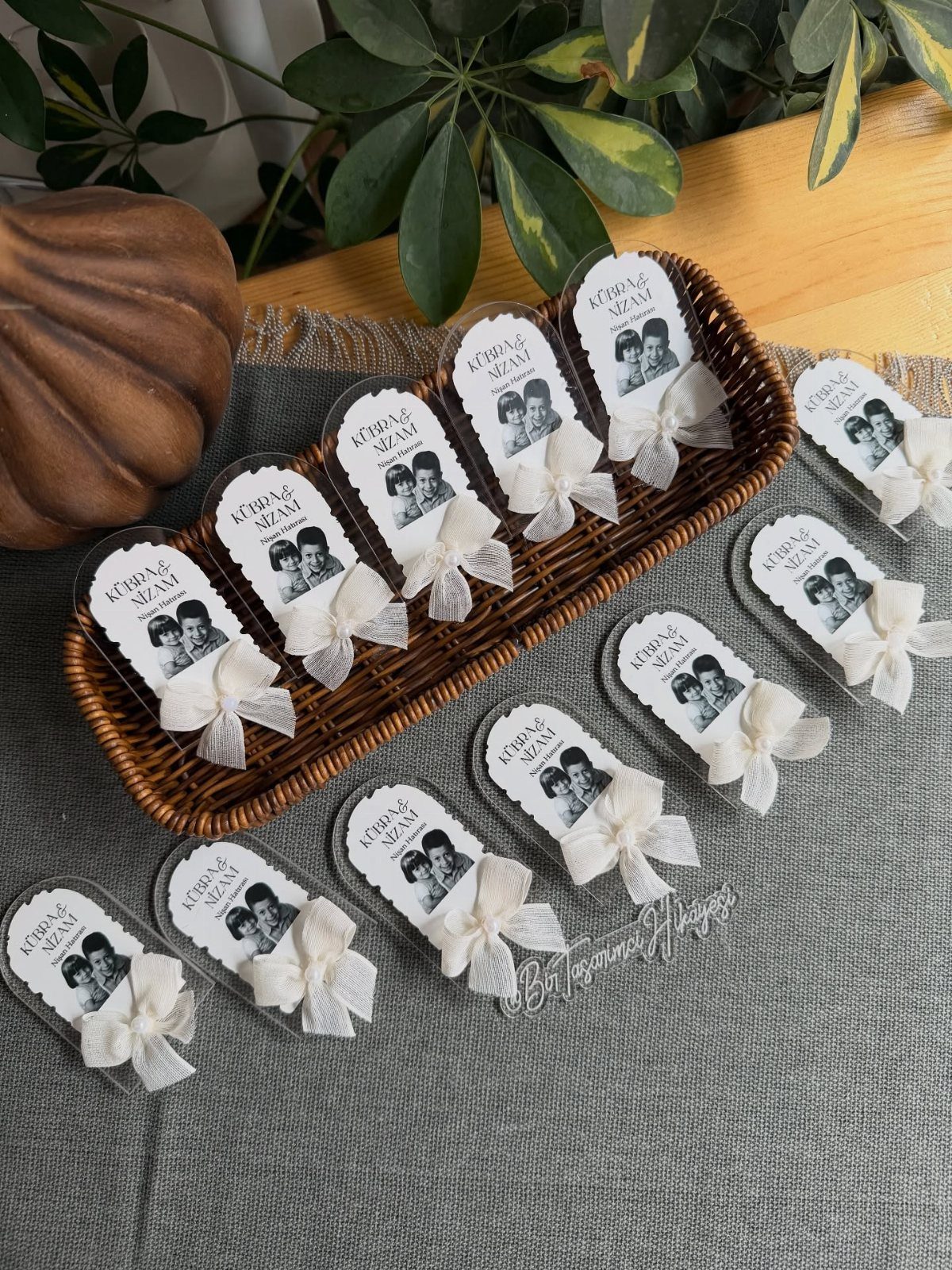 Oval acrylic ornaments with couple photos and white bows in a wicker basket.