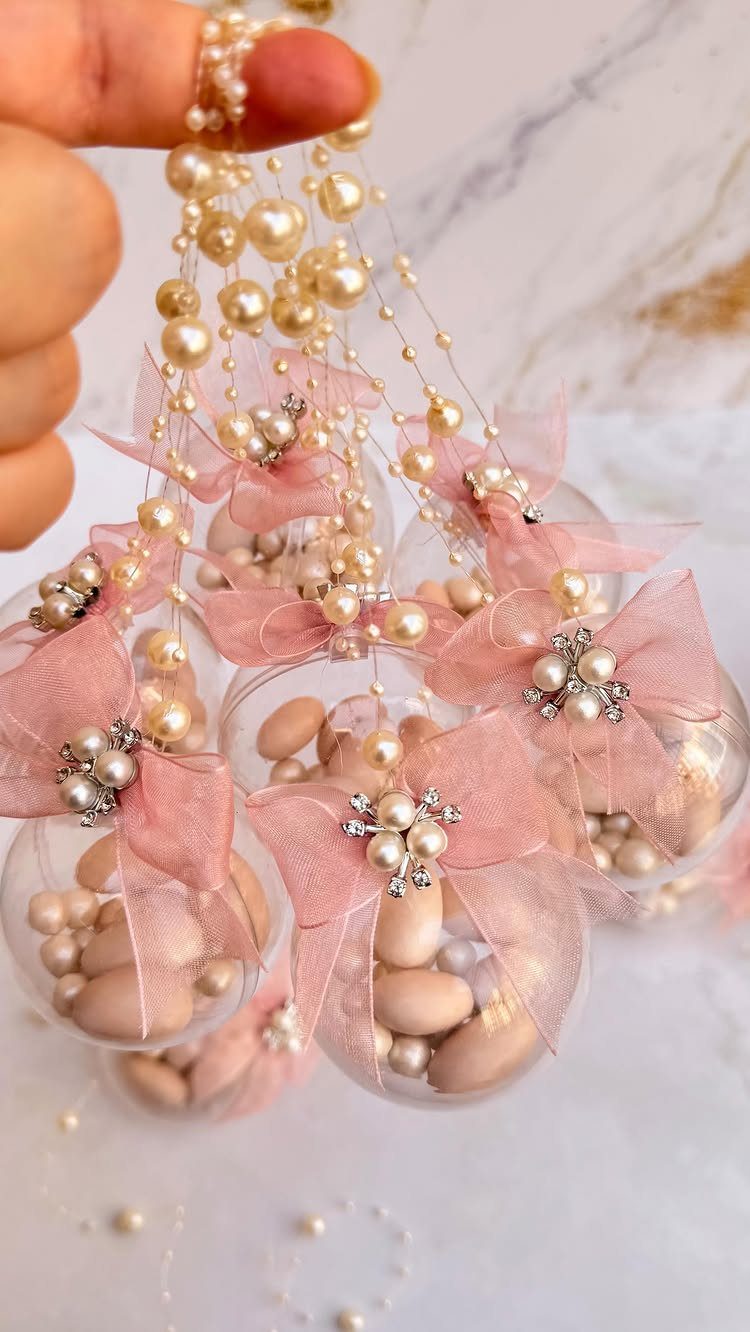 Clear glass ball ornaments filled with almonds and pearls with pink bows.