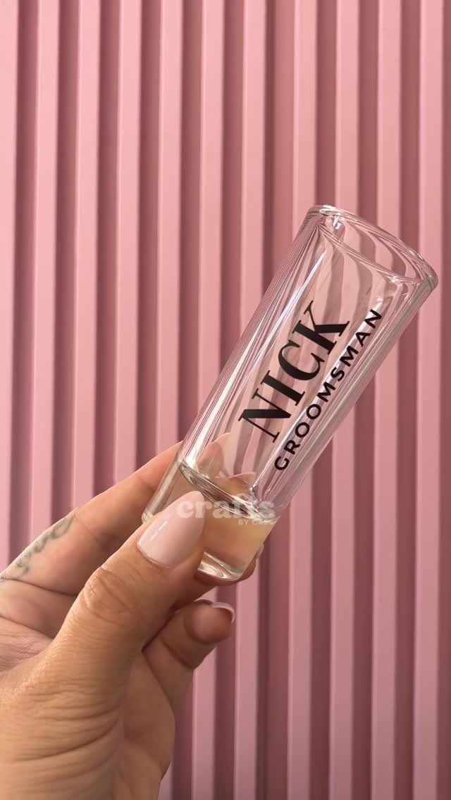 Clear glass shot glass with Nick Groomsman text held against pink ribbed background