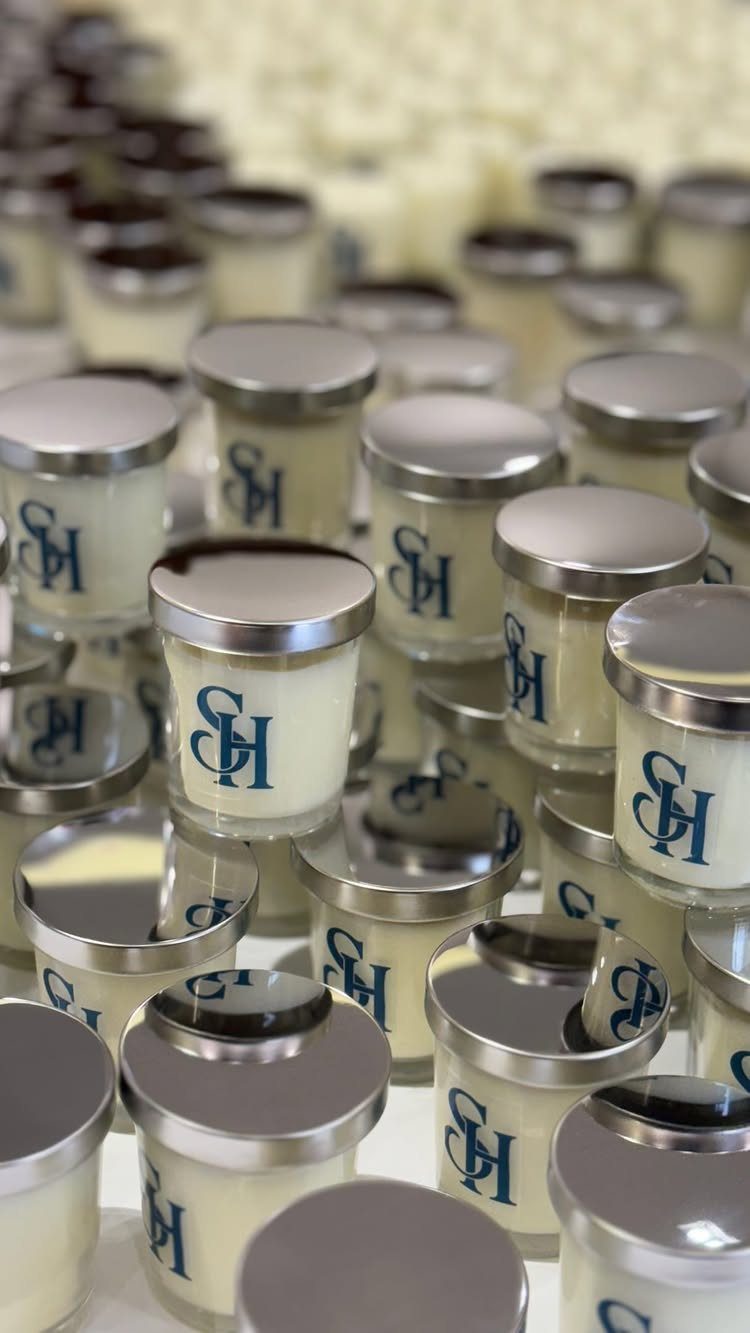 Small white scented candles in frosted jars with silver lids and blue monograms.