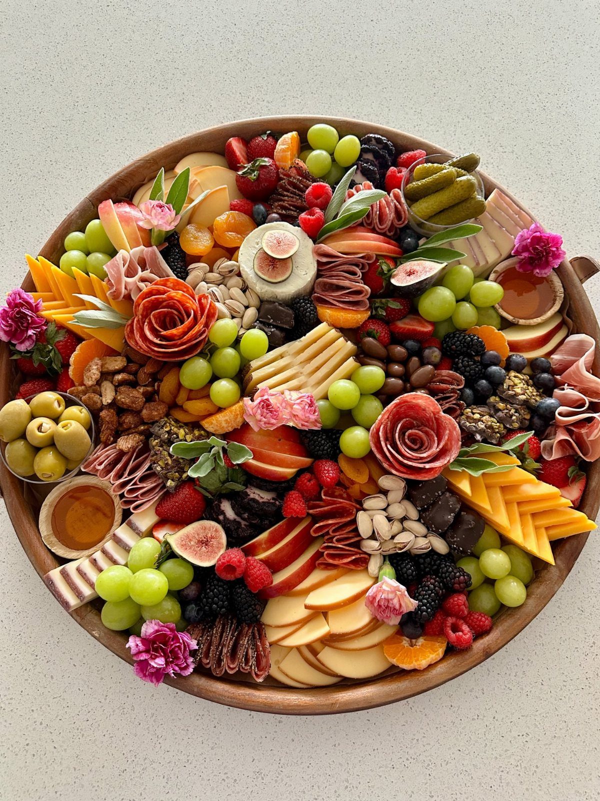 Round wooden charcuterie board overflowing with assorted cheeses, meats, fruits, and nuts.