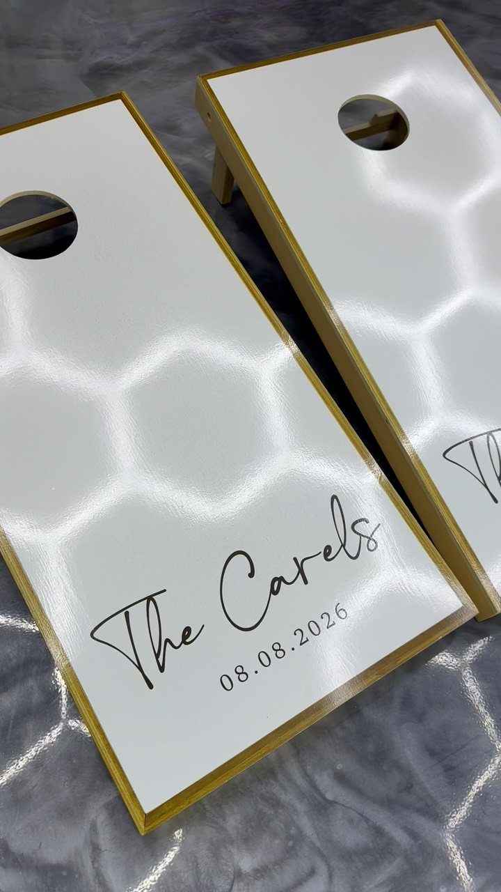 Custom white cornhole boards with gold trim and personalized wedding date text.