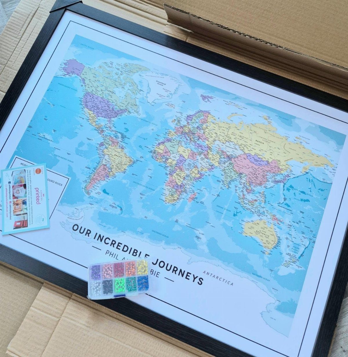 Framed world map for tracking travels with colorful push pins and personalized text.