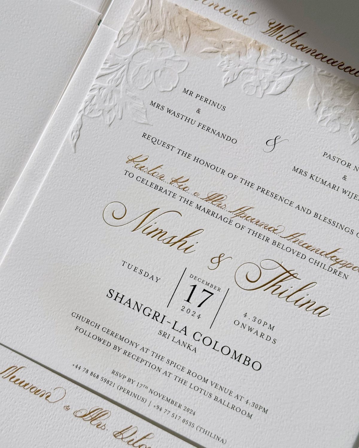 White wedding invitation with gold calligraphy names and embossed floral details.