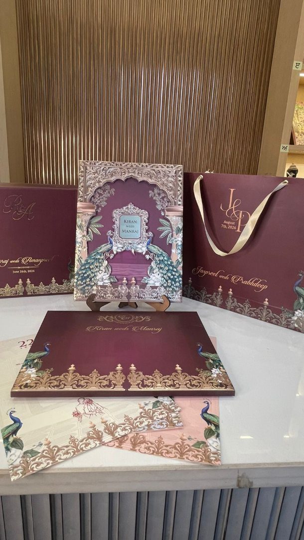 Luxury burgundy and gold wedding invitation set with ornate peacock designs and patterns.