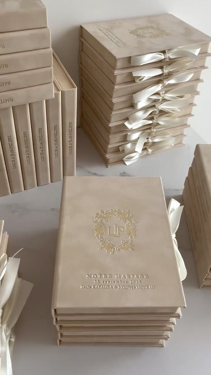 Cream wedding invitation boxes with gold foil crests and white satin ribbons.