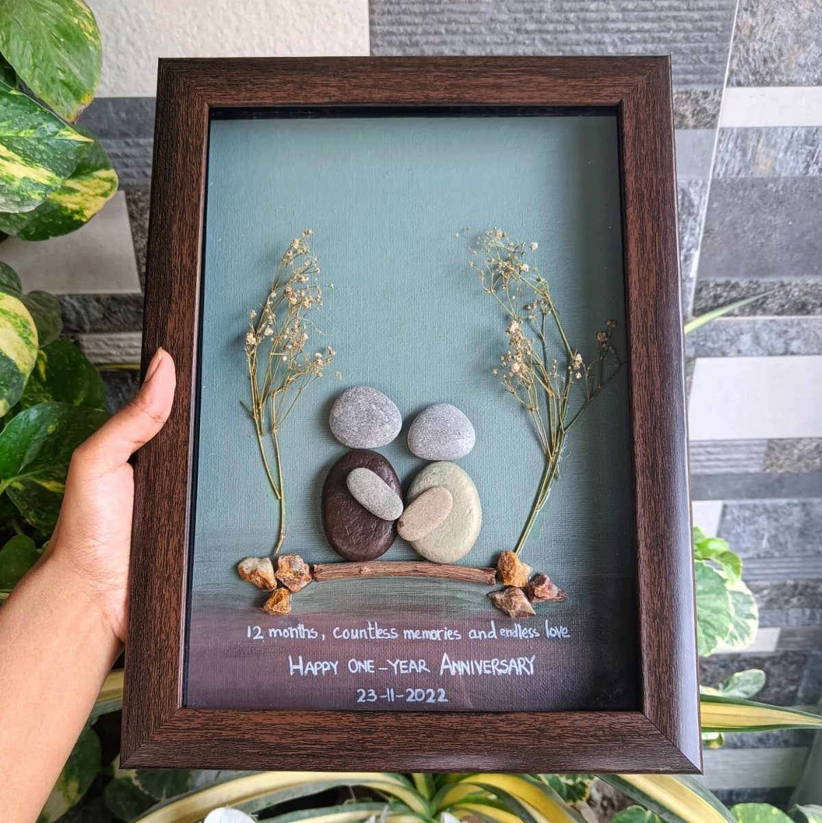 Pebble art of a couple sitting on a branch in a wooden frame.